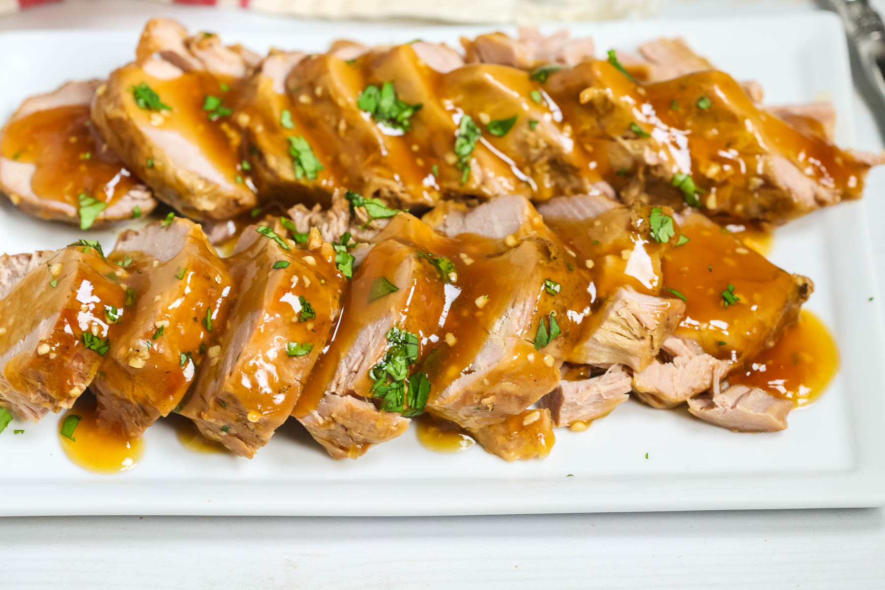 A white platter with pork tenderloin on it with a gravy on top.