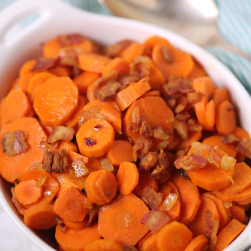 Glazed Bacon Carrots in a white casserole dish with a spoon on the side.