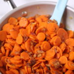 A bpwl of carrots with a spoon in them.