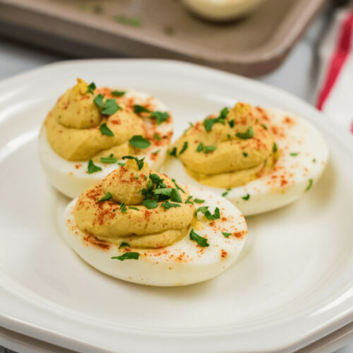 Million Dollar Deviled Eggs garnished with paprika and parsley on a white plate.