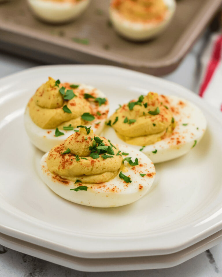 Million Dollar Deviled Eggs garnished with paprika and parsley on a white plate.