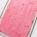 A rectangular glass baking dish filled with a cake topped with a luscious layer of raspberry buttercream frosting.