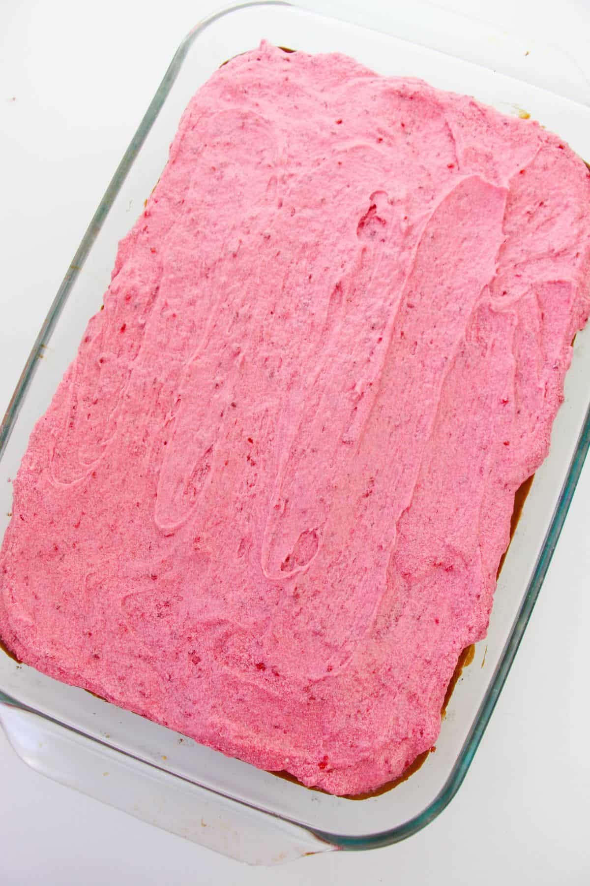 A rectangular glass baking dish filled with a cake topped with a luscious layer of raspberry buttercream frosting.