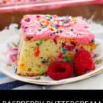 A slice of cake topped with raspberry buttercream frosting and sprinkles sits on a plate with fresh raspberries; a tray of raspberry buttercream cake is in the background.
