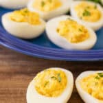 A plate of shrimp deviled eggs garnished with parsley, served on a blue plate with a blurred background.