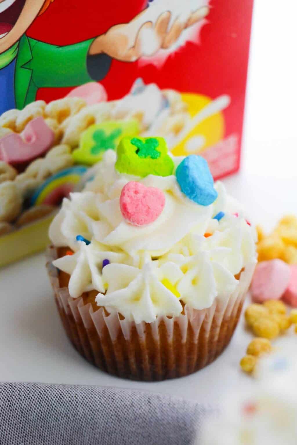 A dessert topped with white frosting and colorful cereal pieces sits cheerfully in front of a red cereal box.