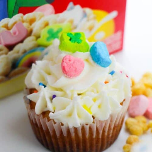 A dessert topped with white frosting and colorful cereal pieces sits cheerfully in front of a red cereal box.
