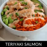 A delightful teriyaki salmon bowl featuring spicy mayo, edamame, grated carrots, and a sprinkle of sesame seeds and green onions.