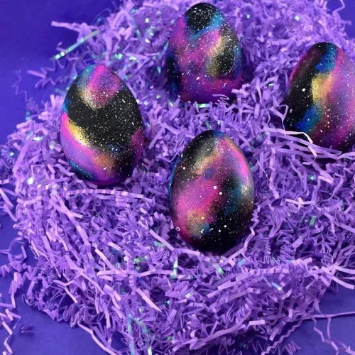 Eggs painted in a purple, blue and black galaxy pattern.