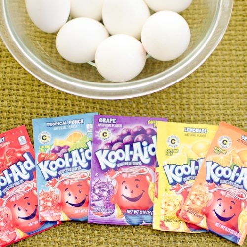 A bowl of plain white eggs surrounded by an assortment of kool aid packets.