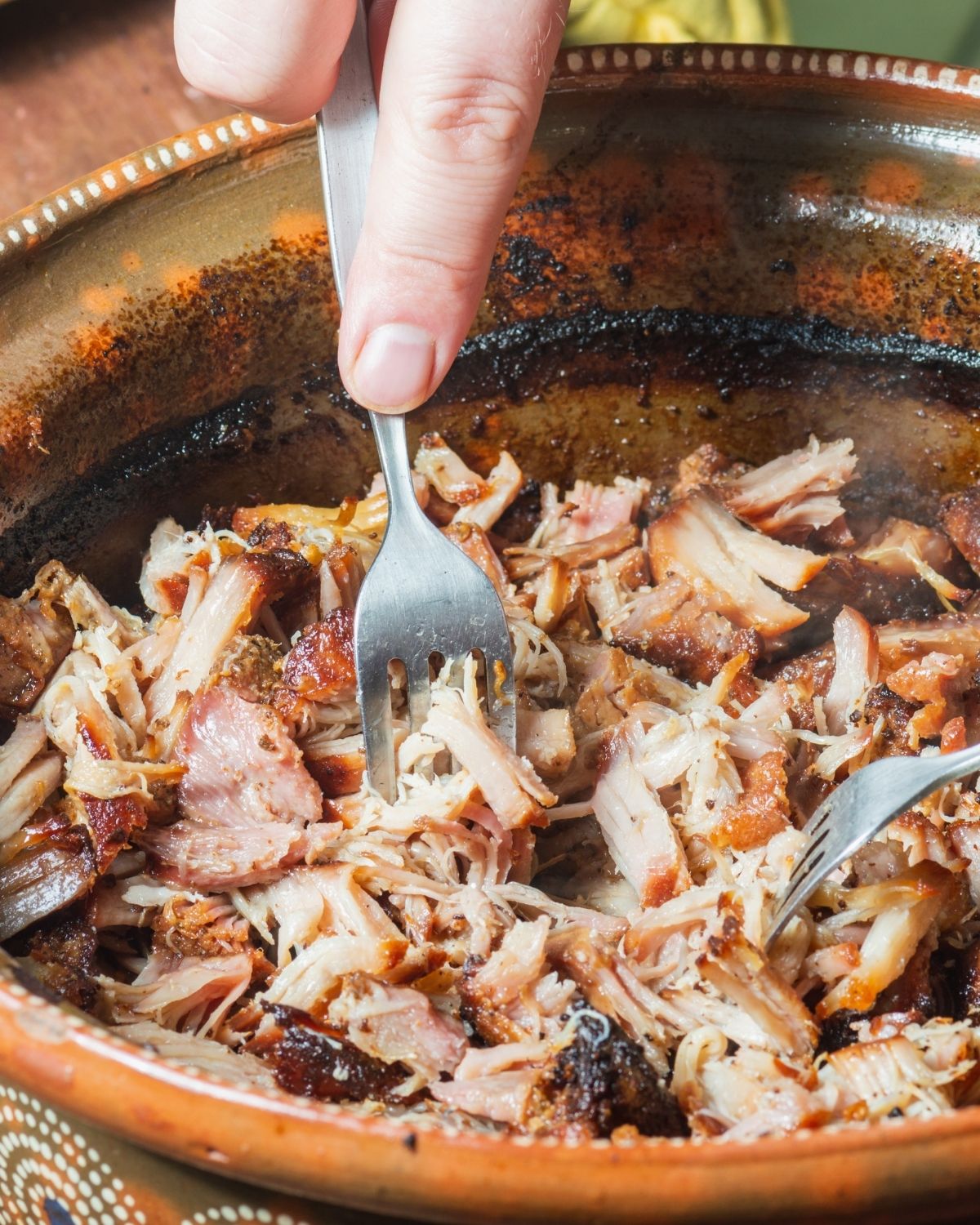 Cooked pulled pork in the crock pot being shredded by a fork.