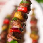 A close-up of a skewer with grilled vegetables and meat, including bell peppers, mushrooms, and onion, garnished with herbs—these delectable steak kabobs are a feast for the eyes and the palate.