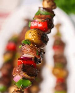 A close-up of a skewer with grilled vegetables and meat, including bell peppers, mushrooms, and onion, garnished with herbs—these delectable steak kabobs are a feast for the eyes and the palate.