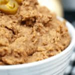 Close-up of a bowl of instant pot refried beans topped with sliced jalapeños, served on a table.