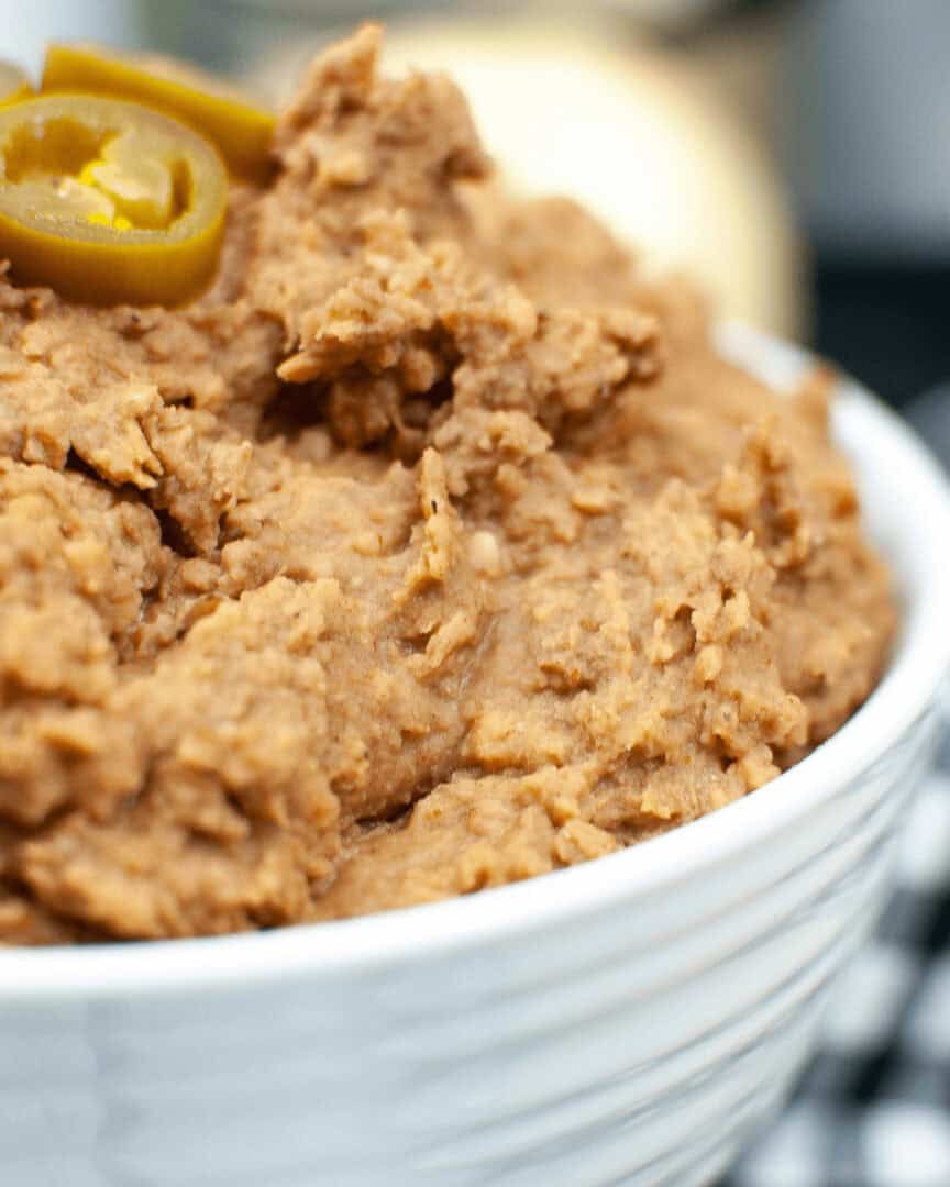 Close-up of a bowl of instant pot refried beans topped with sliced jalapeños, served on a table.