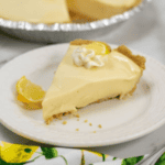 A slice of Lemon Icebox Pie with a dollop of whipped cream on a white plate, with additional lemon slices on the side.