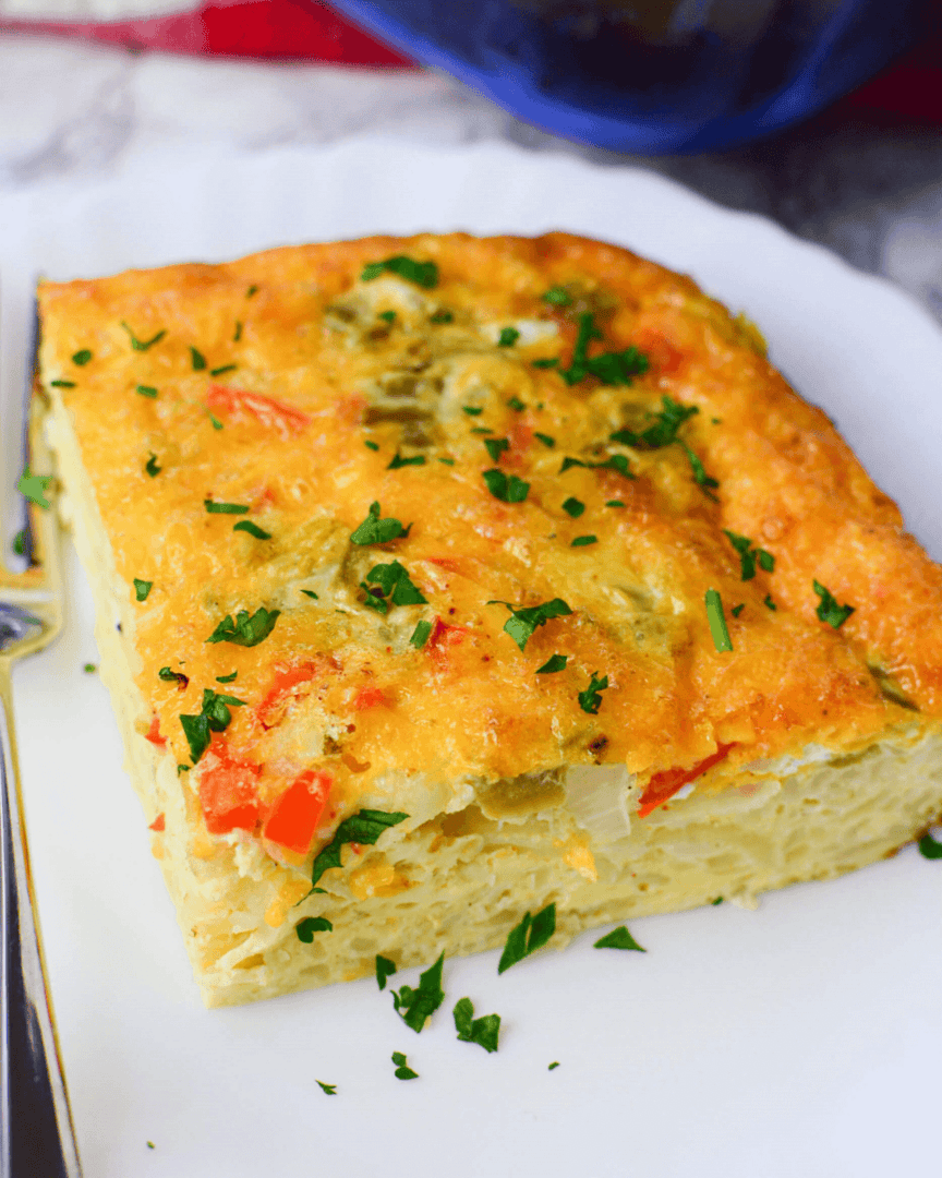 A slice of Mexican breakfast casserole garnished with fresh herbs on a white plate.