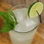 A refreshing lime moonshine drink garnished with a sprig of mint on a wooden surface.