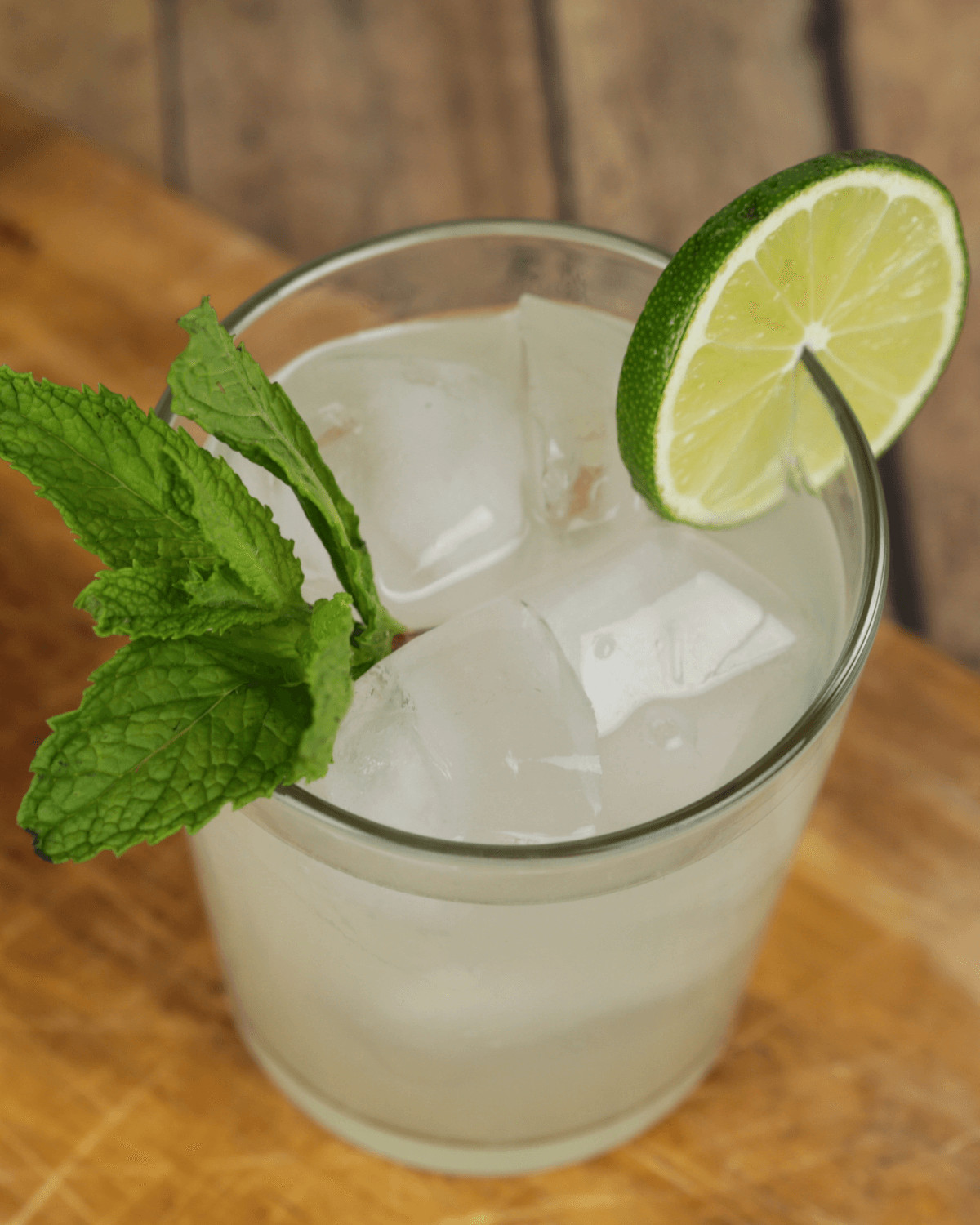 A refreshing lime moonshine drink garnished with a sprig of mint on a wooden surface.