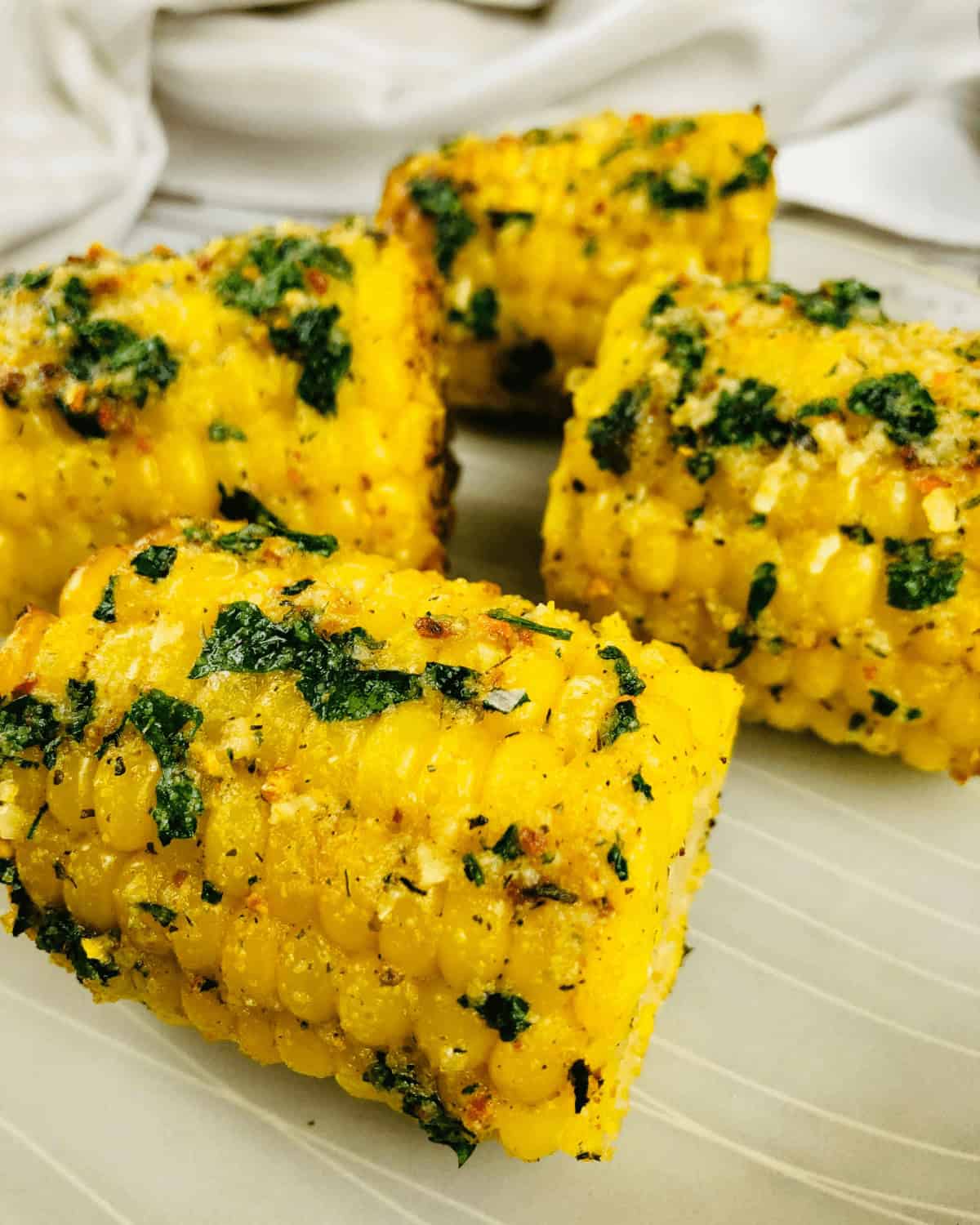 Close-up of air fryer corn on the cob pieces, garnished with chopped herbs and spices, arranged on a white plate.