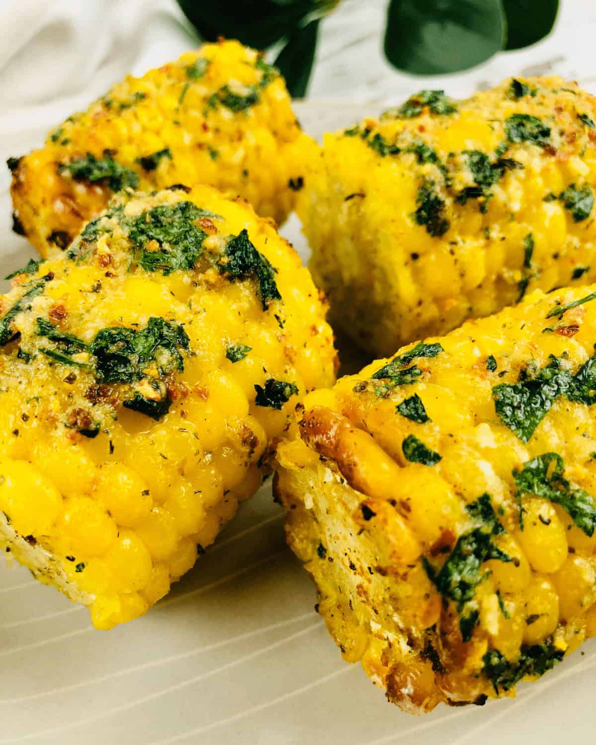 Four pieces of air fryer corn on the cob, topped with herbs and spices, arranged on a plate.