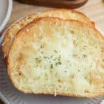 Two slices of Air Fryer Garlic Bread topped with melted cheese and herbs are served on a white plate.
