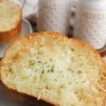 A slice topped with melted cheese and herbs on a plate, with salt and pepper shakers in the background.