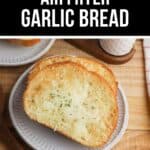 Three slices of Air Fryer Garlic Bread with melted cheese and herbs sit on a white plate, placed on a wooden table with a wooden spoon and a cup in the background.