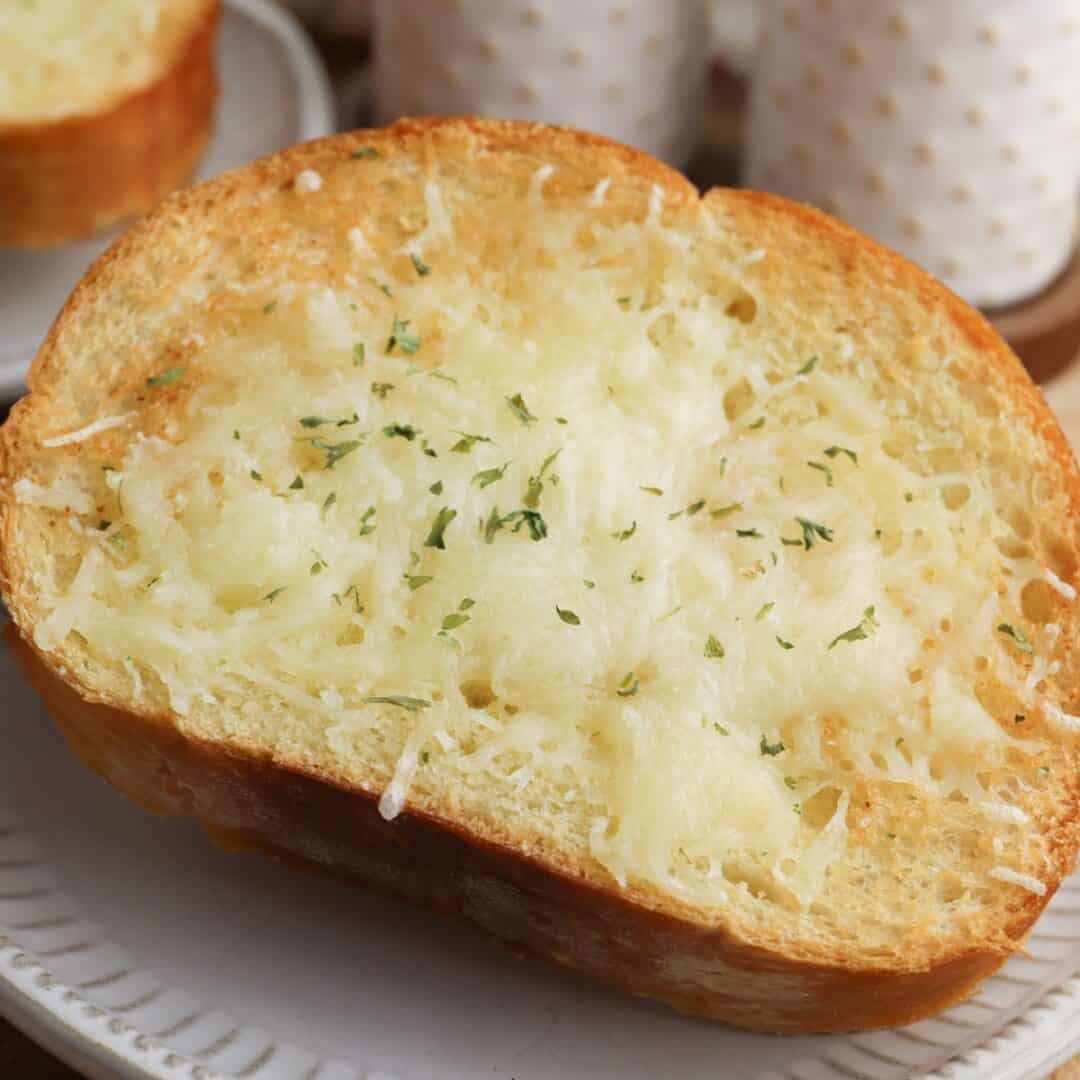 A slice of toasted Air Fryer Garlic Bread topped with melted cheese and sprinkled with herbs, served on a white plate.