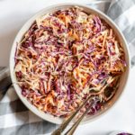 A bowl of slaw with utensils.