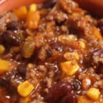 A bowl of hearty beef and bean chili brimming with ground meat, black beans, corn, bell peppers, and tomatoes.