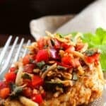 Grilled chicken breast topped with a savory bruschetta chicken recipe of diced tomatoes, red onions, fresh basil, and shredded cheese on a clear glass plate with a fork.