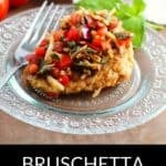 A piece of bruschetta chicken, inspired by a classic bruschetta chicken recipe, is topped with diced tomatoes, onions, and herbs, served on a clear glass plate with a fork and fresh basil in the background.