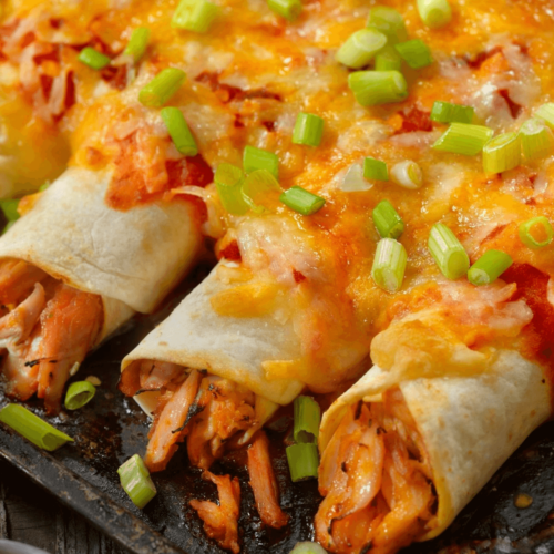 Cheesy chicken enchiladas topped with melted cheese and chopped green onions, served on a black plate.
