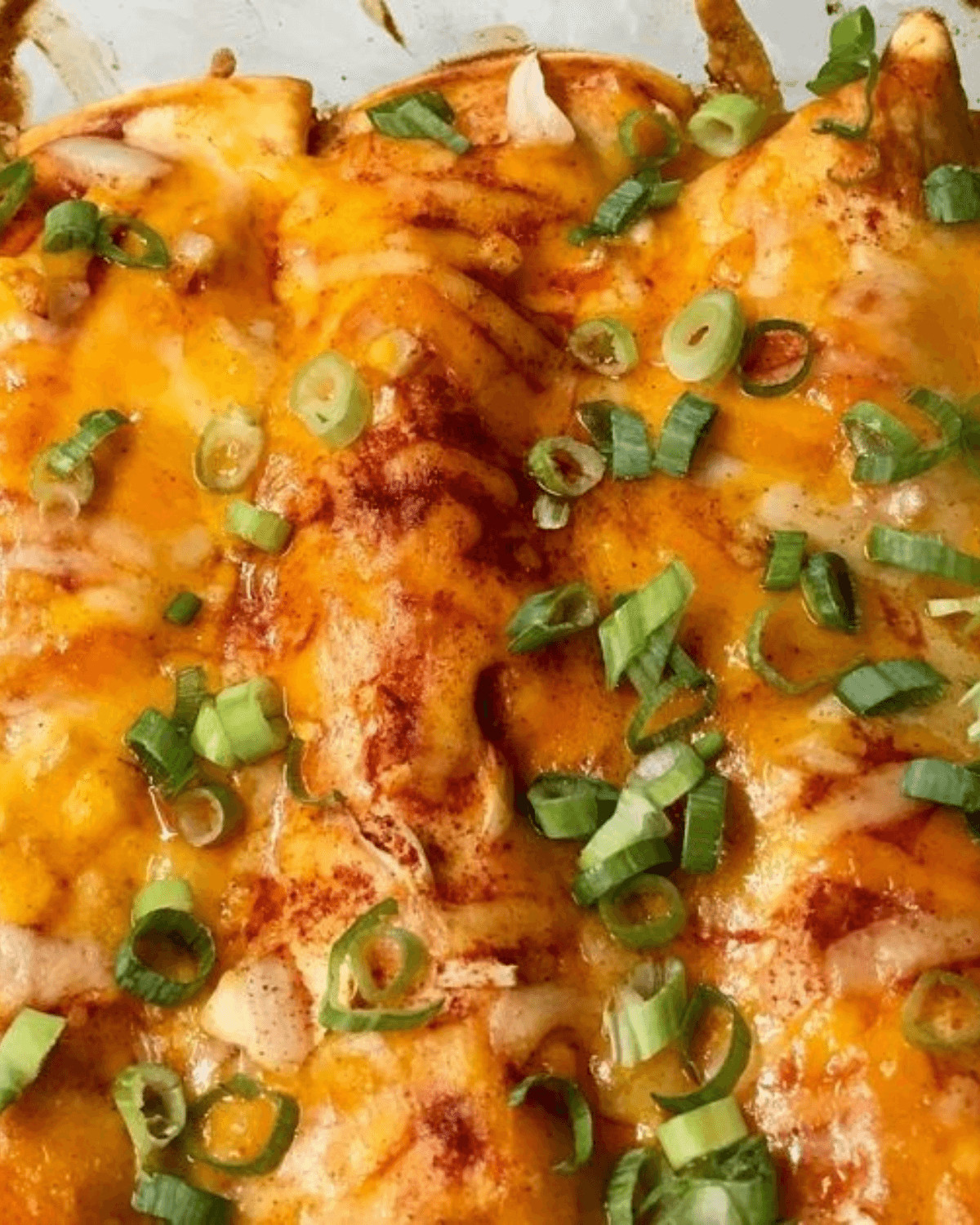 A closeup of the dish topped with melted cheese and green onions, garnished with red spices.