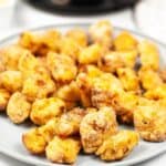 A plate filled with golden-brown, crispy copycat Chick-fil-A nuggets sits in front of an air fryer on a white surface.