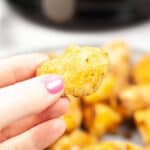 A hand with pink nail polish holds a golden-brown snack.