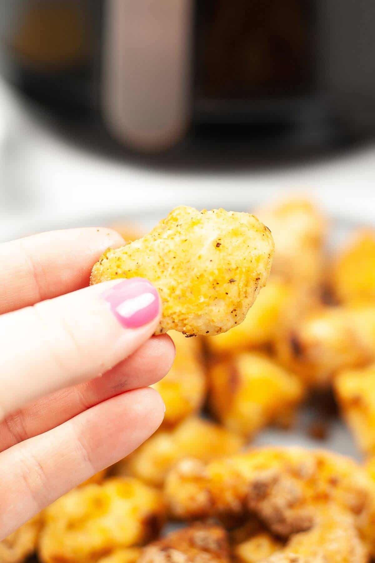 A hand with pink nail polish holds a golden-brown snack.