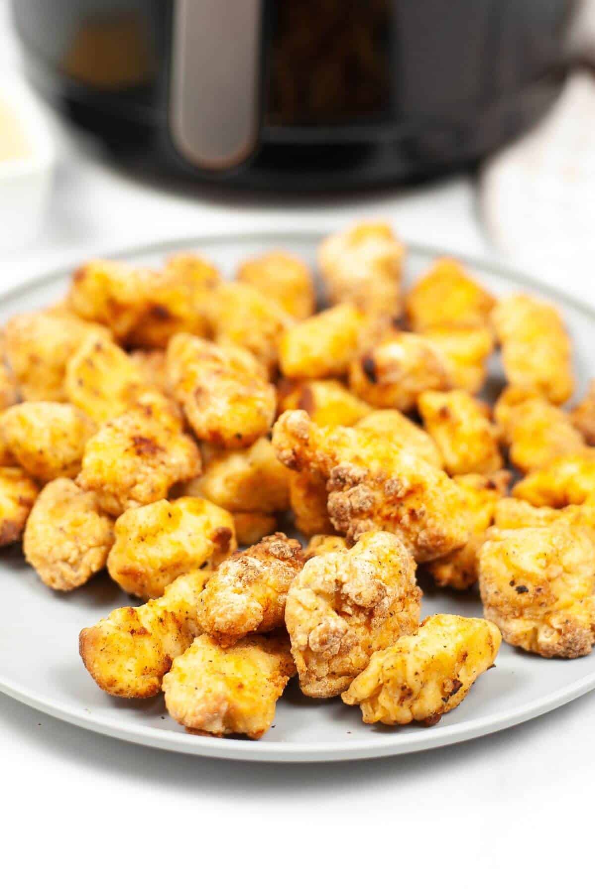 A gray plate filled with crispy, golden brown copycat Chick-fil-A nuggets sits on a white surface, with an air fryer visible in the background.