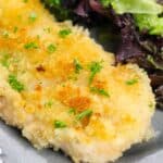 A classic Chicken Milanese—breaded and baked chicken breast garnished with chopped herbs—served on a plate with a side of mixed green salad.