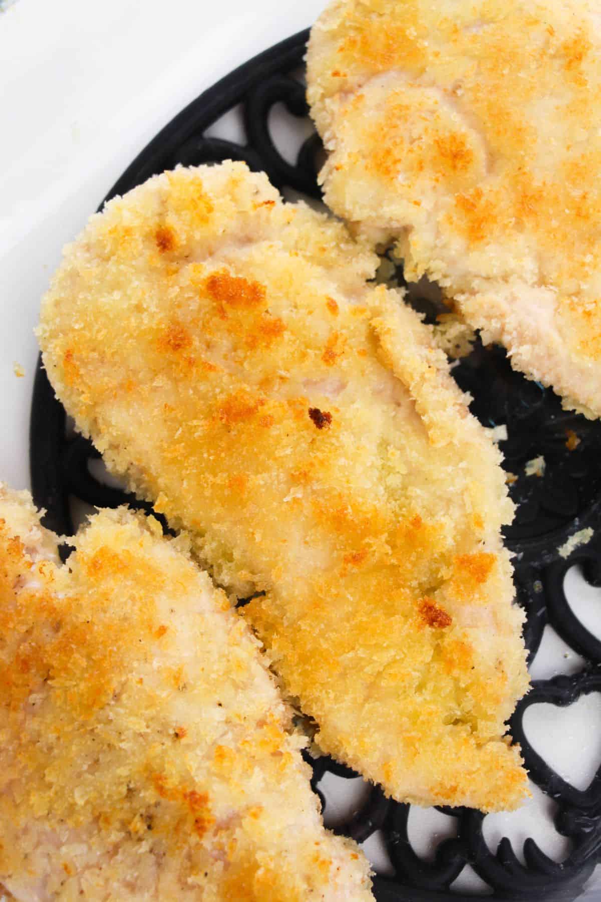 Chicken Milanese: Breaded and baked chicken breasts with a golden, crispy coating on a black decorative trivet.