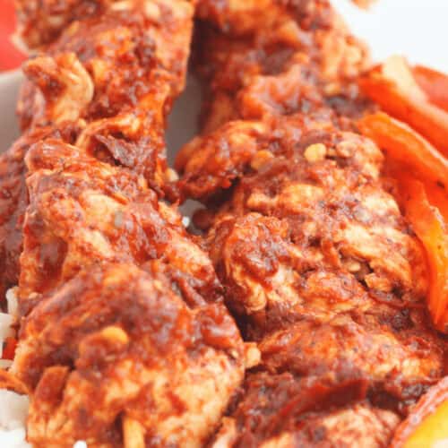 Oven Chicken Kabobs coated in a thick red sauce, served on a bed of white rice with sliced bell peppers.