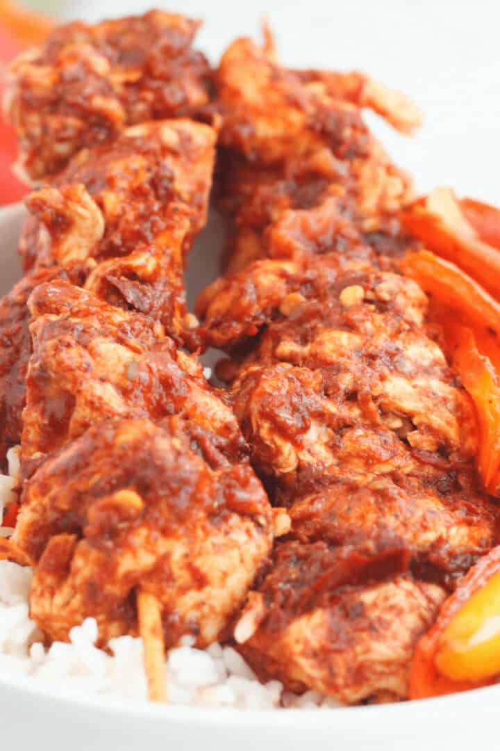 Oven Chicken Kabobs coated in a thick red sauce, served on a bed of white rice with sliced bell peppers.