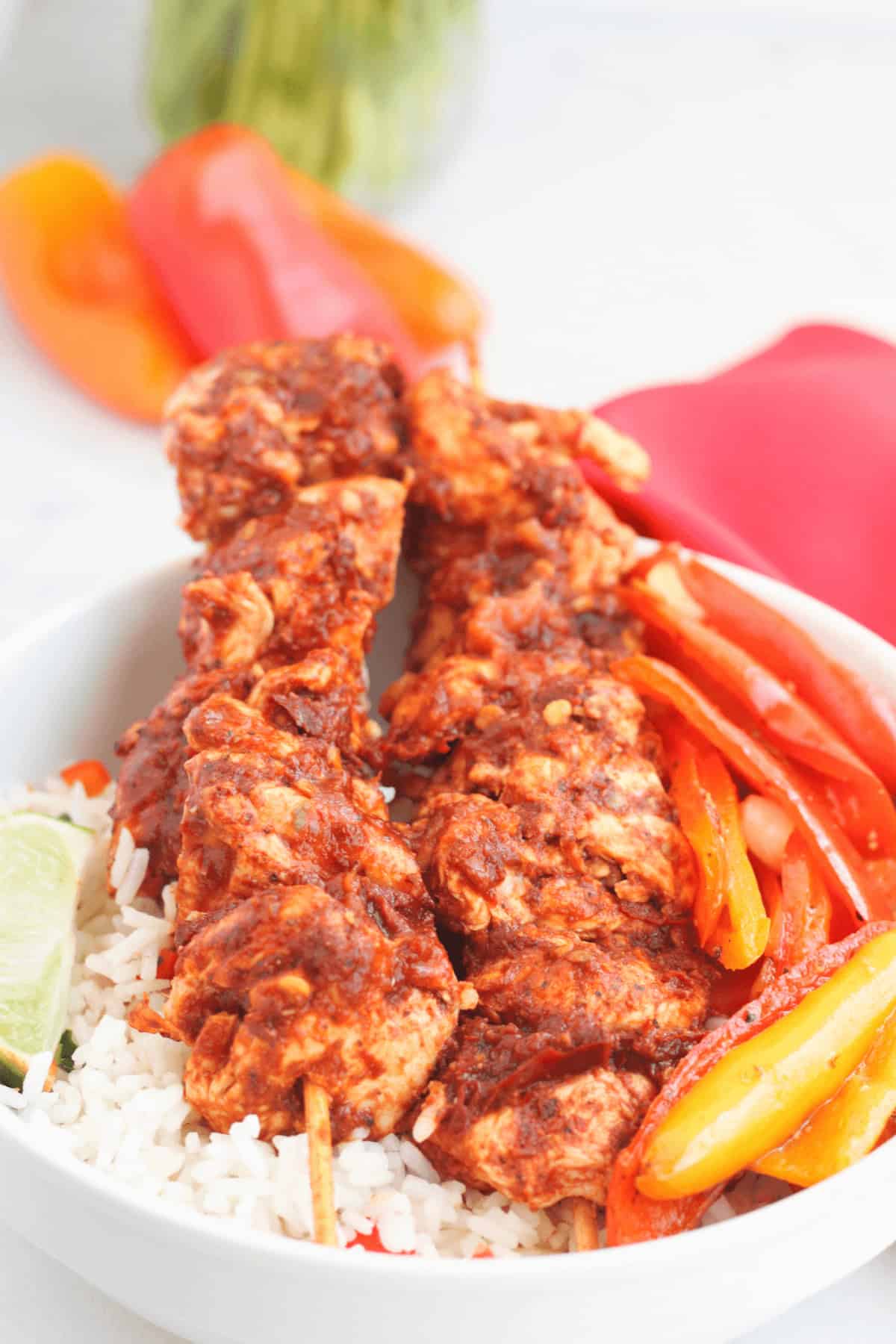 A bowl of rice topped with succulent oven chicken kabobs, grilled to perfection alongside seasoned red and yellow bell peppers, and garnished with a lime wedge.