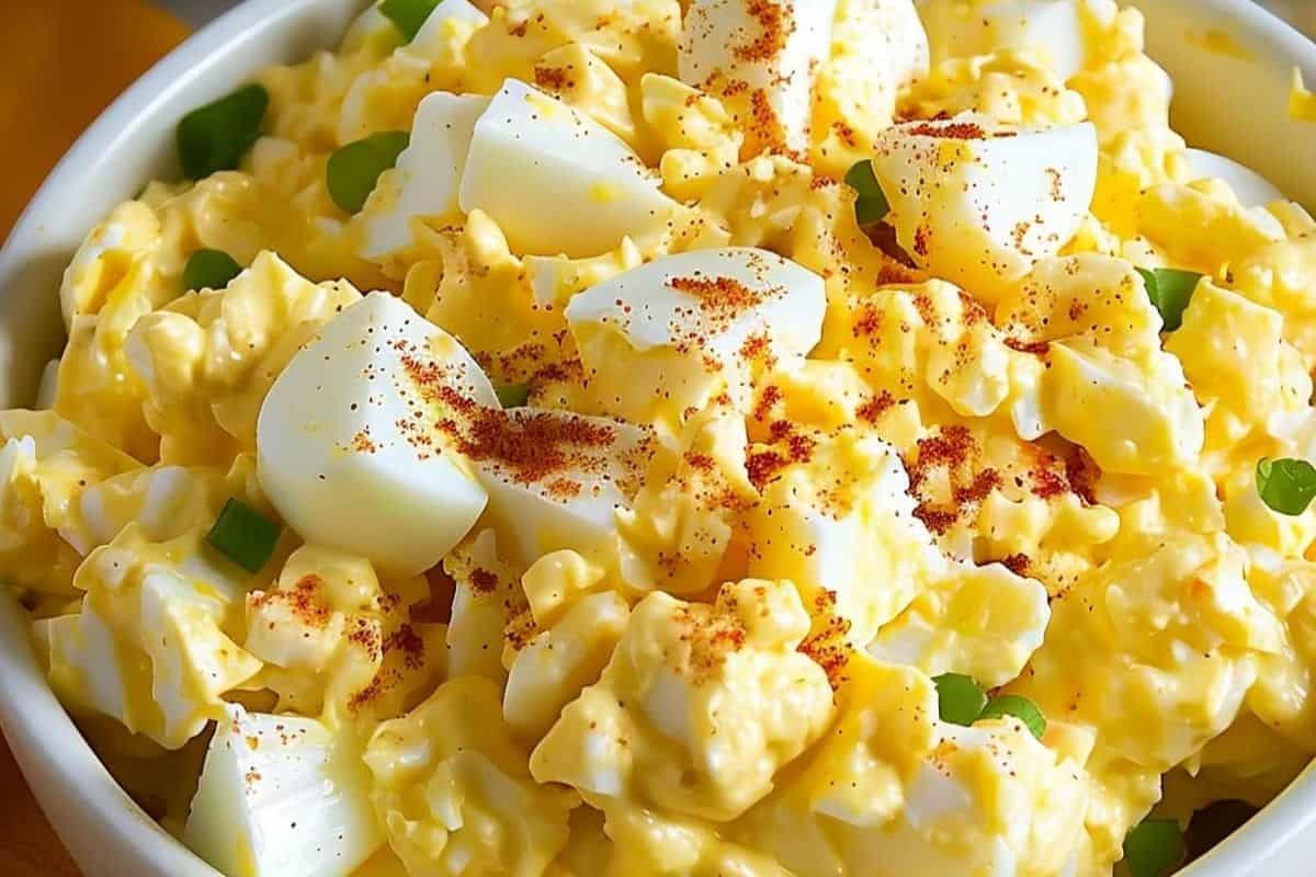 Discover an easy egg salad recipe featuring a bowl of creamy goodness, topped with paprika and chopped green onions.