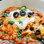 A hearty bowl of Crockpot Chicken Enchilada Casserole, topped with melted cheese, sour cream, sliced black olives, and fresh cilantro.