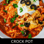 Close-up of Crockpot Chicken Enchilada Casserole topped with melted cheese, sliced black olives, sour cream, and cilantro in a white bowl. Text overlay says, "Crock Pot Chicken Enchilada Casserole.