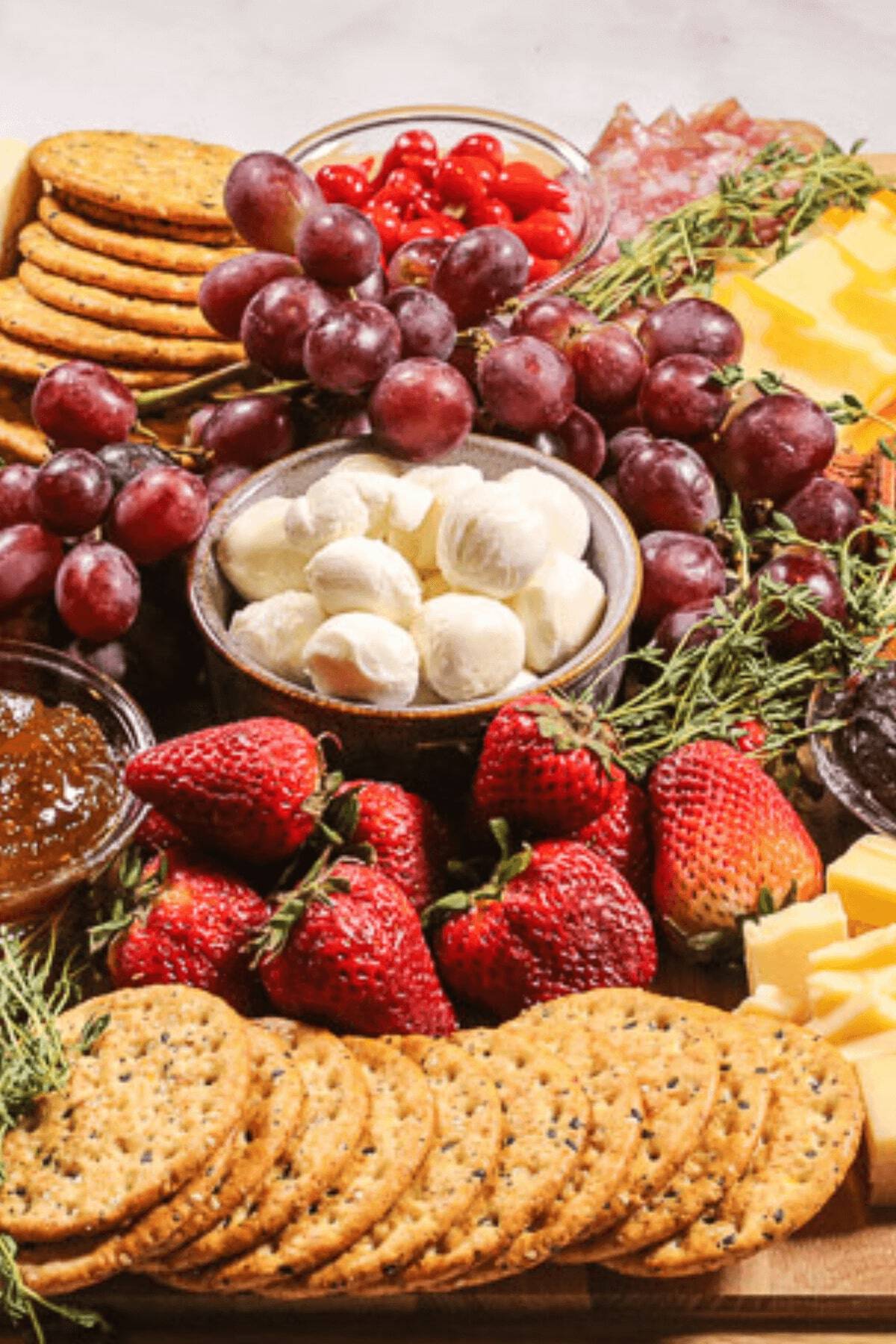 An easy charcuterie board featuring crackers, grapes, mozzarella balls, strawberries, cheese slices, salami, cherry tomatoes, fig jam, and herbs is perfect for any gathering.