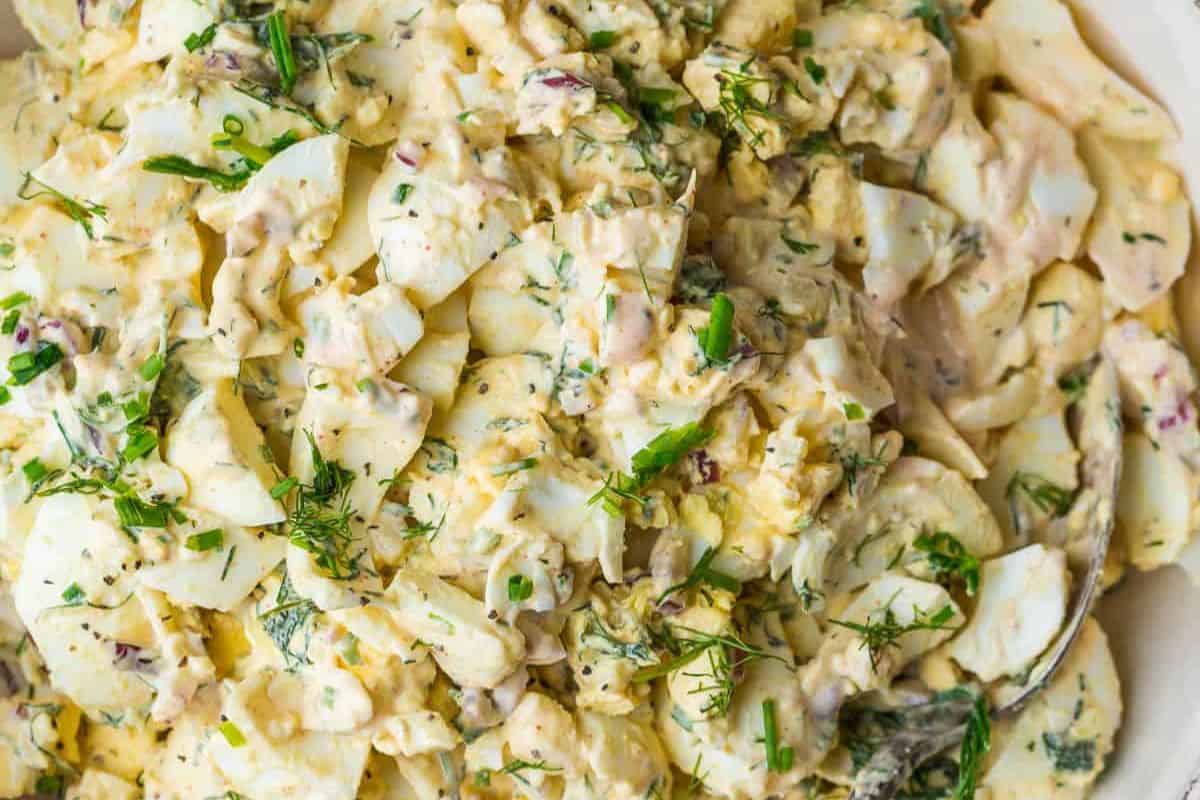 Close-up of a creamy egg salad, one of the many easy egg salad recipes, with chopped herbs and green onions mixed throughout.
