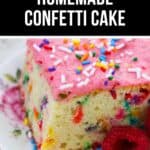 A delightful slice of homemade confetti cake with pink frosting and colorful sprinkles rests on a floral plate, beautifully garnished with fresh raspberries.
